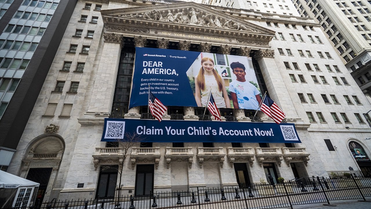The New York Stock Exchange's facade draped with Invest America | Trump Accounts promotional banners across the building.