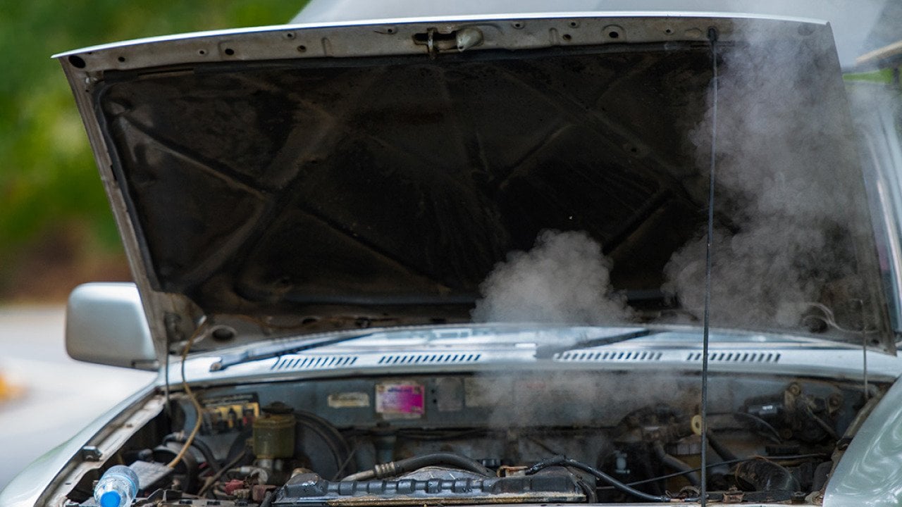 A broken car with overheating and smoking engine parked on the road.