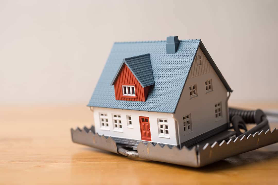 A miniature house within a mouse trap placed in a wooden table.