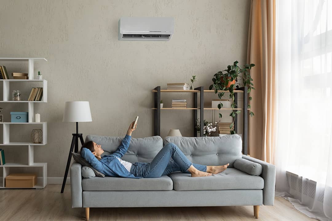 A young woman at home relaxing on the sofa and turning up the AC temperature.