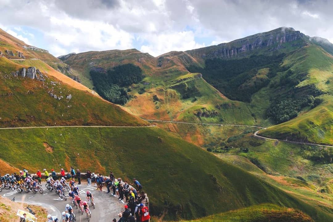 Cyclists descending from a mountain route, with spectators lining up the steep to watch them.
