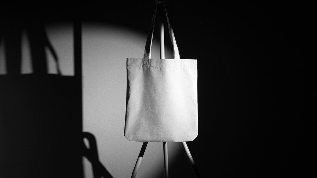 A mockup template of a tote bag on a metal hanger taken in a photo studio.