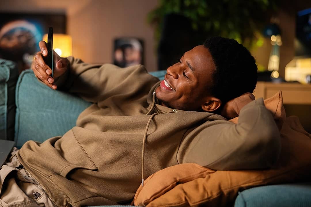 A young man happily checking information on his phone while relaxing at home.