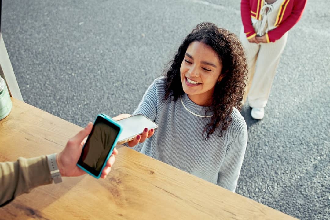 A young woman paying for her food at a food truck using cashless phone payment.