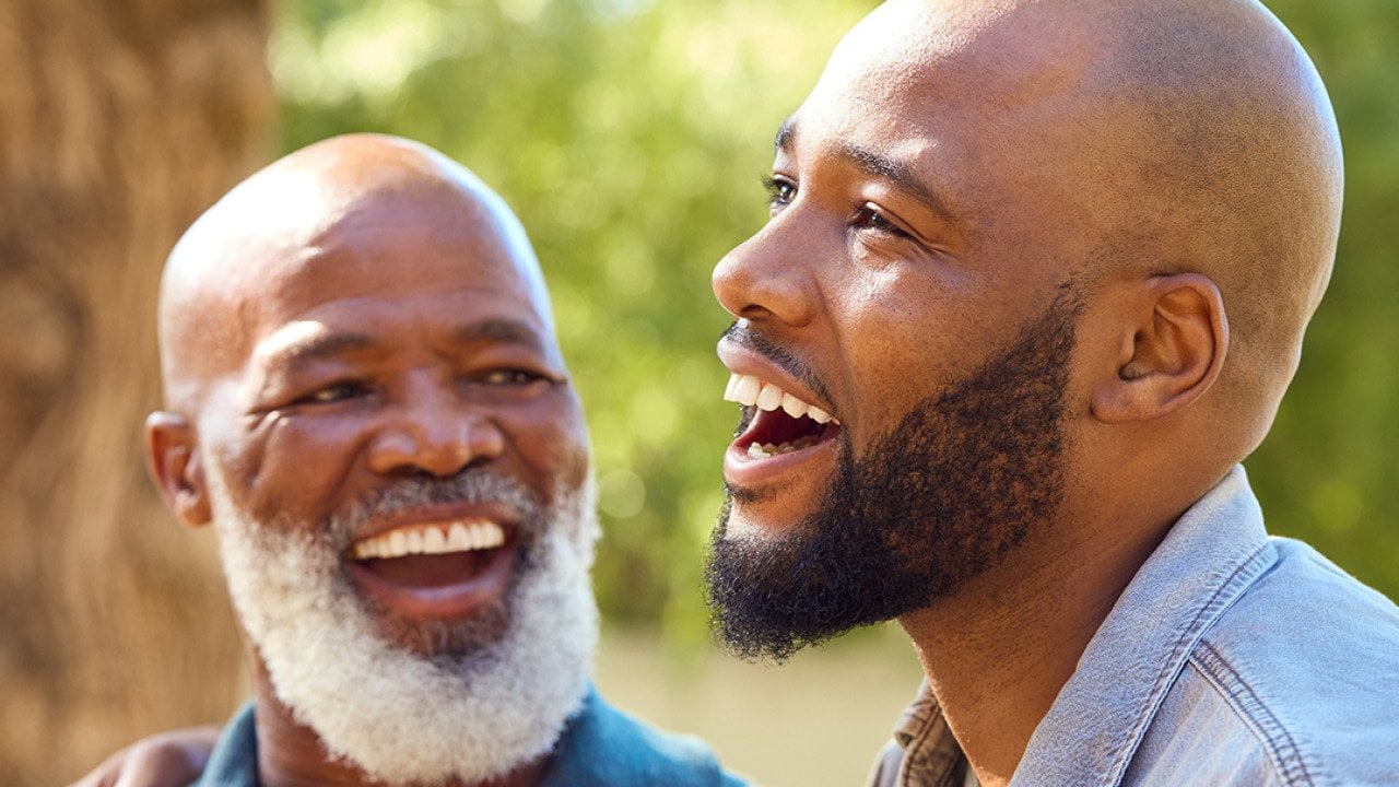 A senior father with his adult son happily engaged in a conversation outdoors.