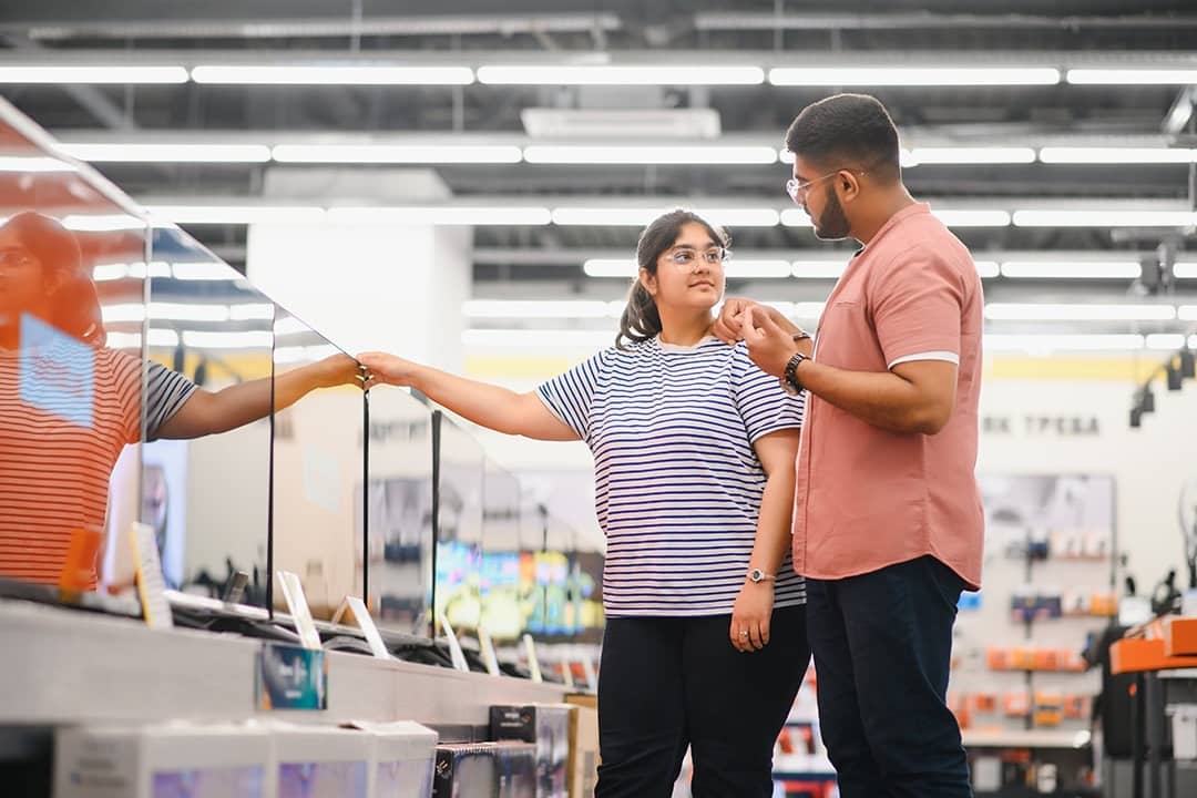 A young couple at an appliance store contemplating to buy a new flatscreen TV.