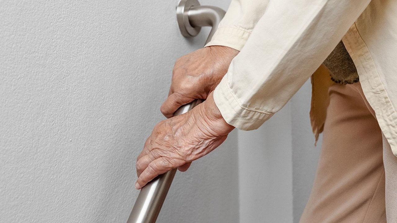 A senior woman holding onto a handrail to safely walk down the stairs.