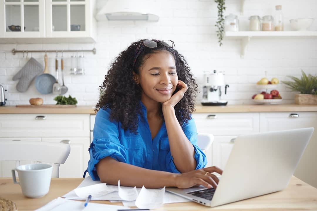 A young woman paying bills online in her home kitchen.