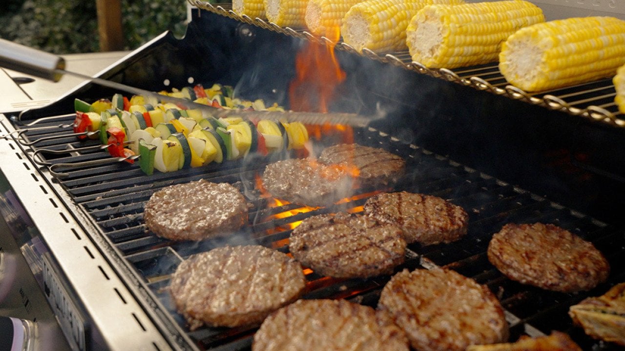 An outdoor gas grill cooking and warming food over flames.