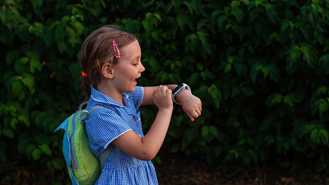 A school kid using her smartwatch outdoors in a park.