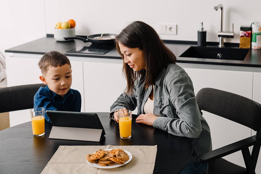 A mother with her young son watching something together on a tablet while having breakfast at home.