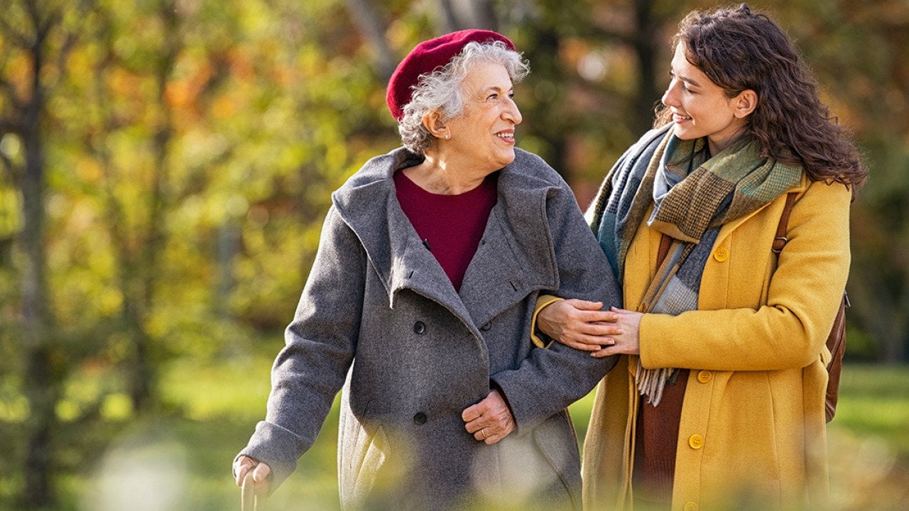 A young woman with her senior grandmother happily walking together at a park.