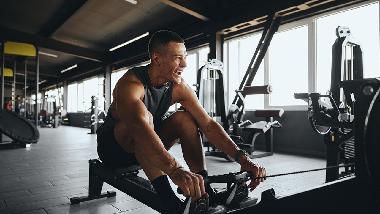 A cheerful man working out using a rowing gym equipment.