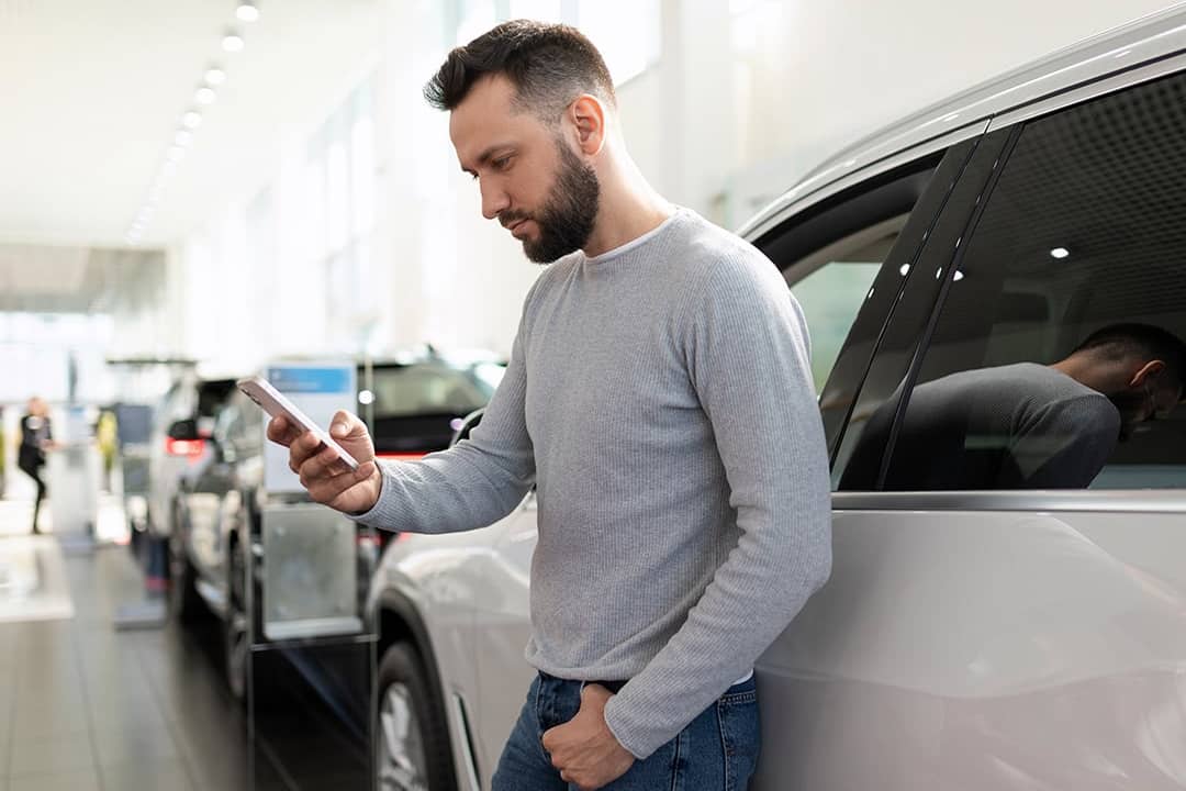 A man at a car dealership looking at information on his phone.