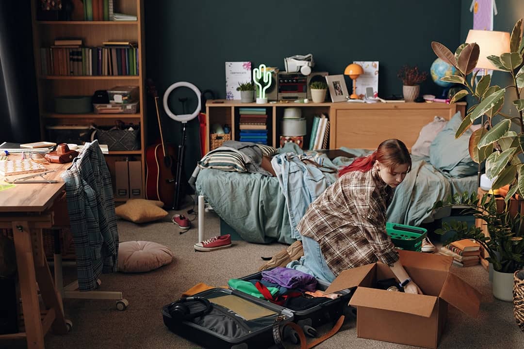 A young woman packing her items into a box in her bedroom.