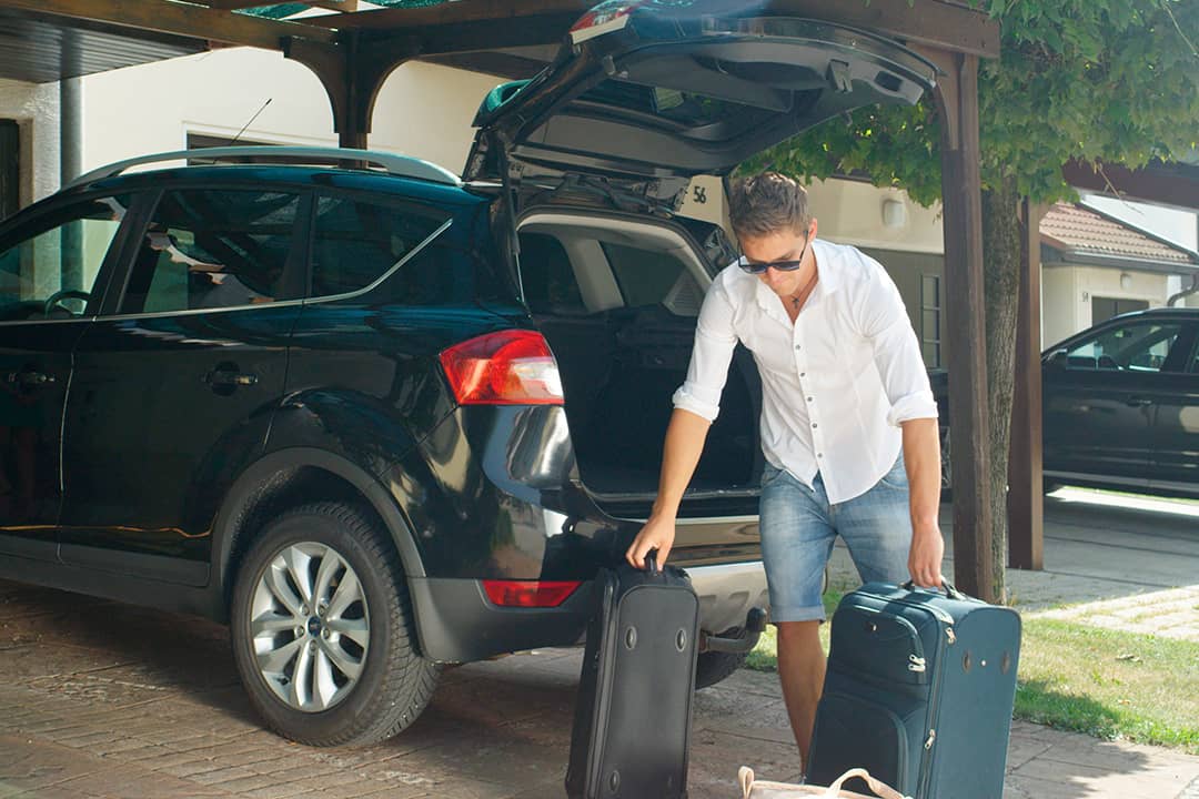 Man unloading heavy suitcases from his SUV's trunk.