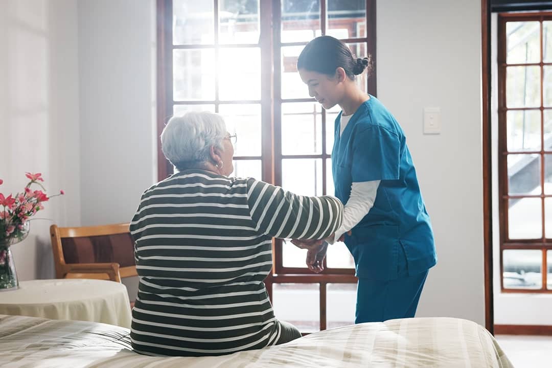 A home nurse assisting an elderly patient from the bed in the morning.