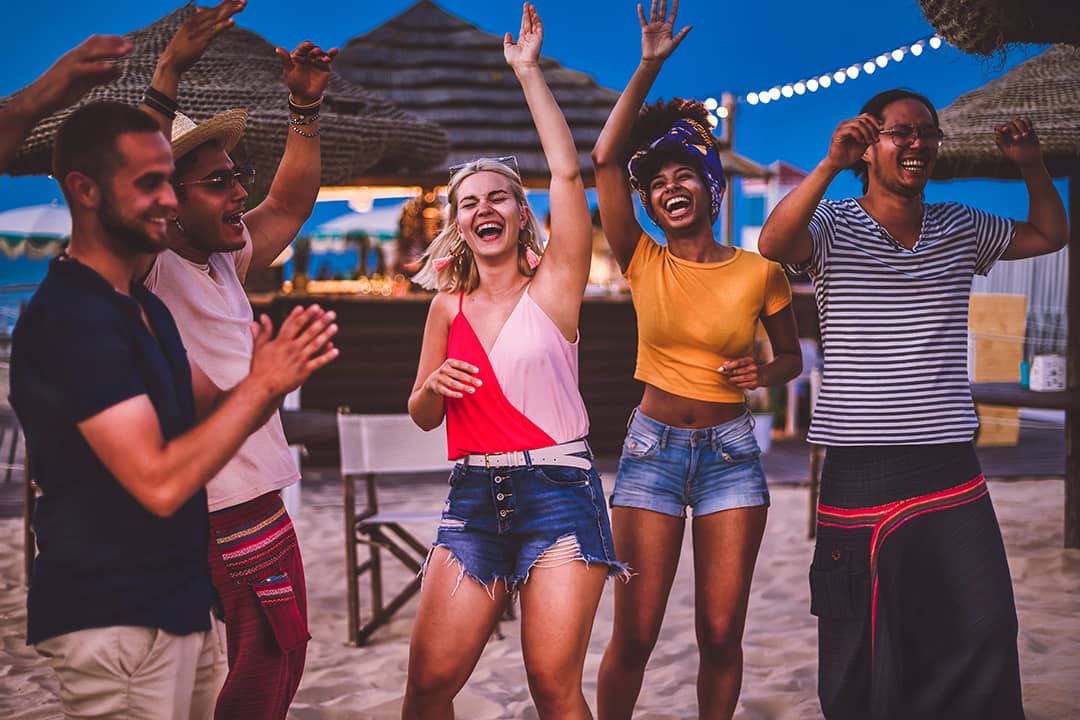 A group of friends dancing happily during a sunset party in the beach.