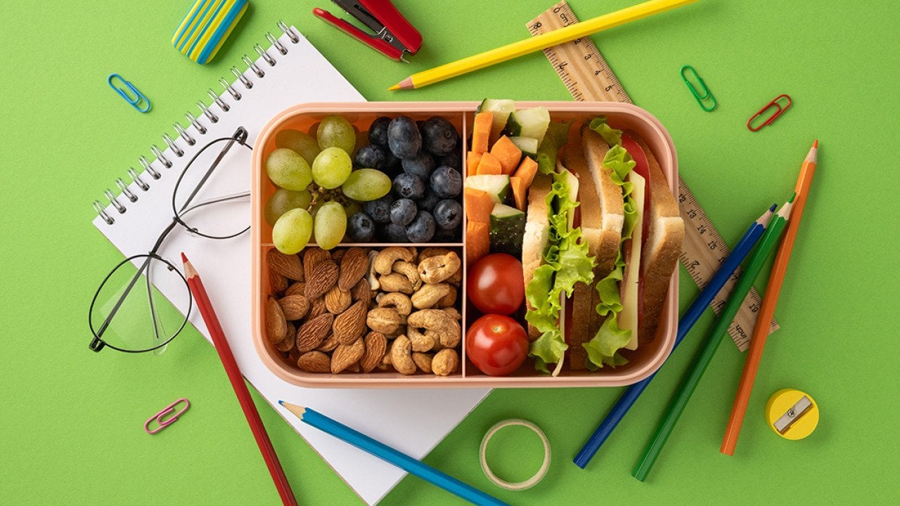 A lunchbox packed with a variety of healthy snacks surrounded by school supplies. 