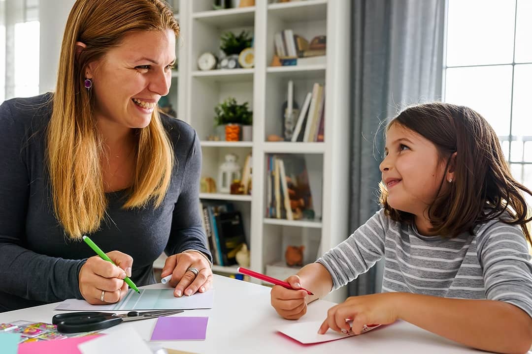 A mother happily teaching her child how to write and to color at home.