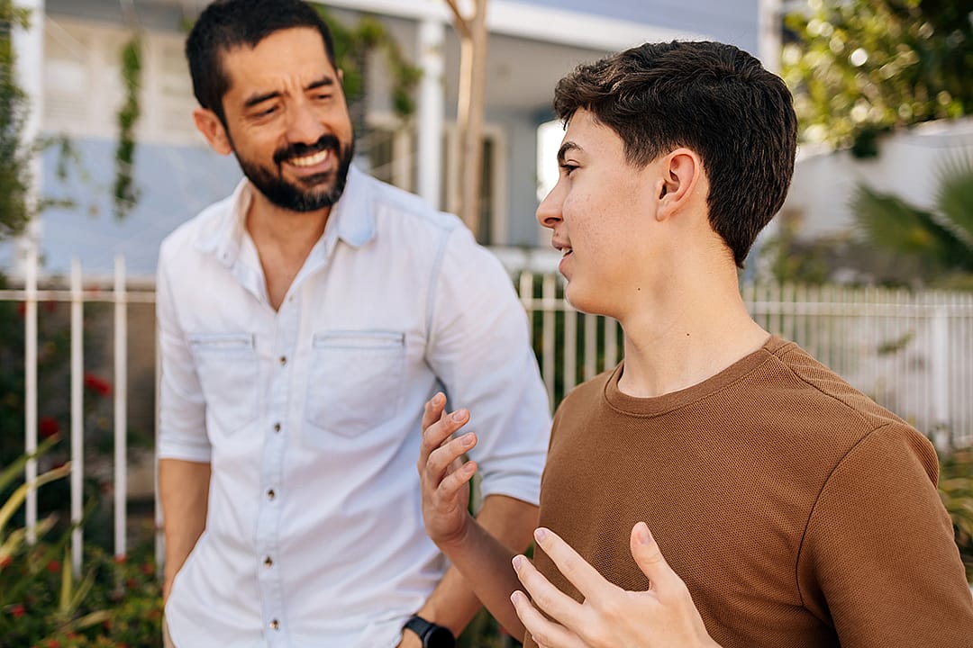A teenage son sharing stories with his father during an outdoor walk.