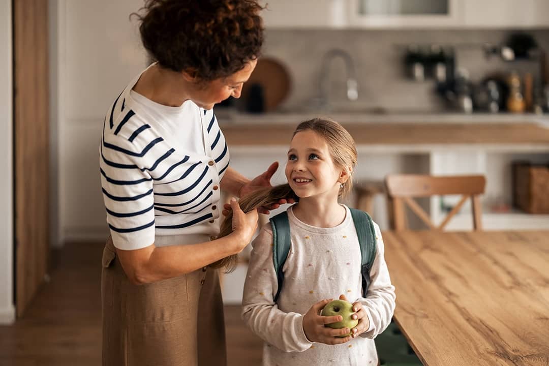 A mother preparing her young daughter to go to school.