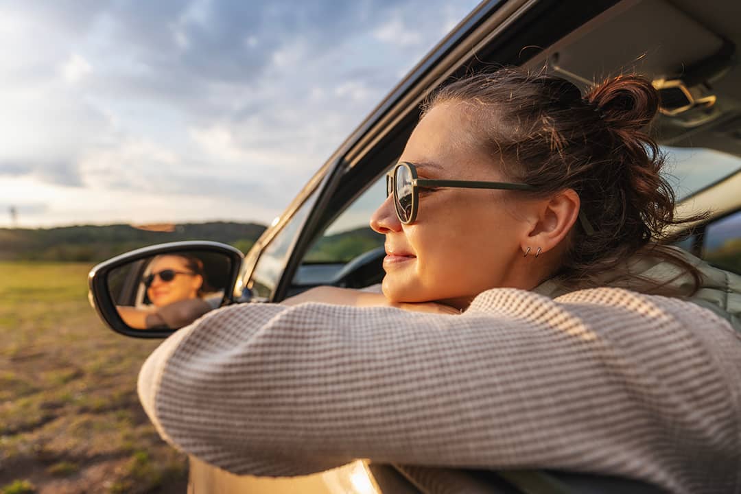 A happy young woman leaning out of a car window during a ride.