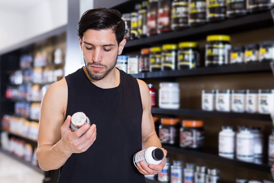 A young man carefully reading the label on a dietary supplement item at a store.
