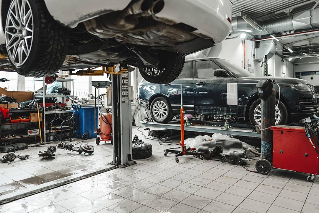 A car raised in a car lift in an auto repair shop.