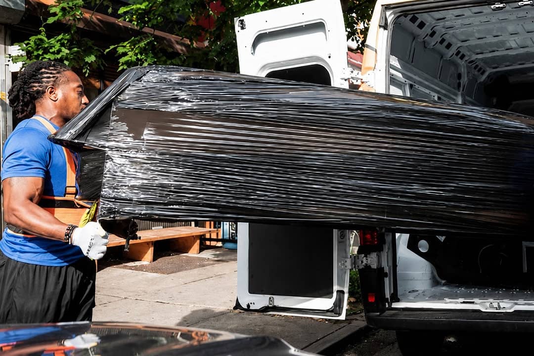 A professional mover loading a large and heavy-wrapped furniture into a delivery van.