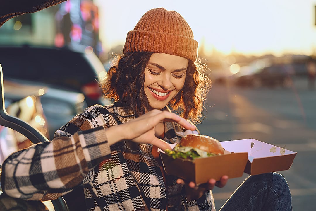 A young woman happily eating a takeout burger.