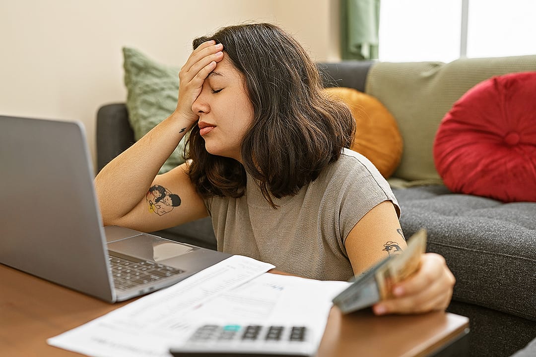 An overwhelmed young woman at home reviewing documents.