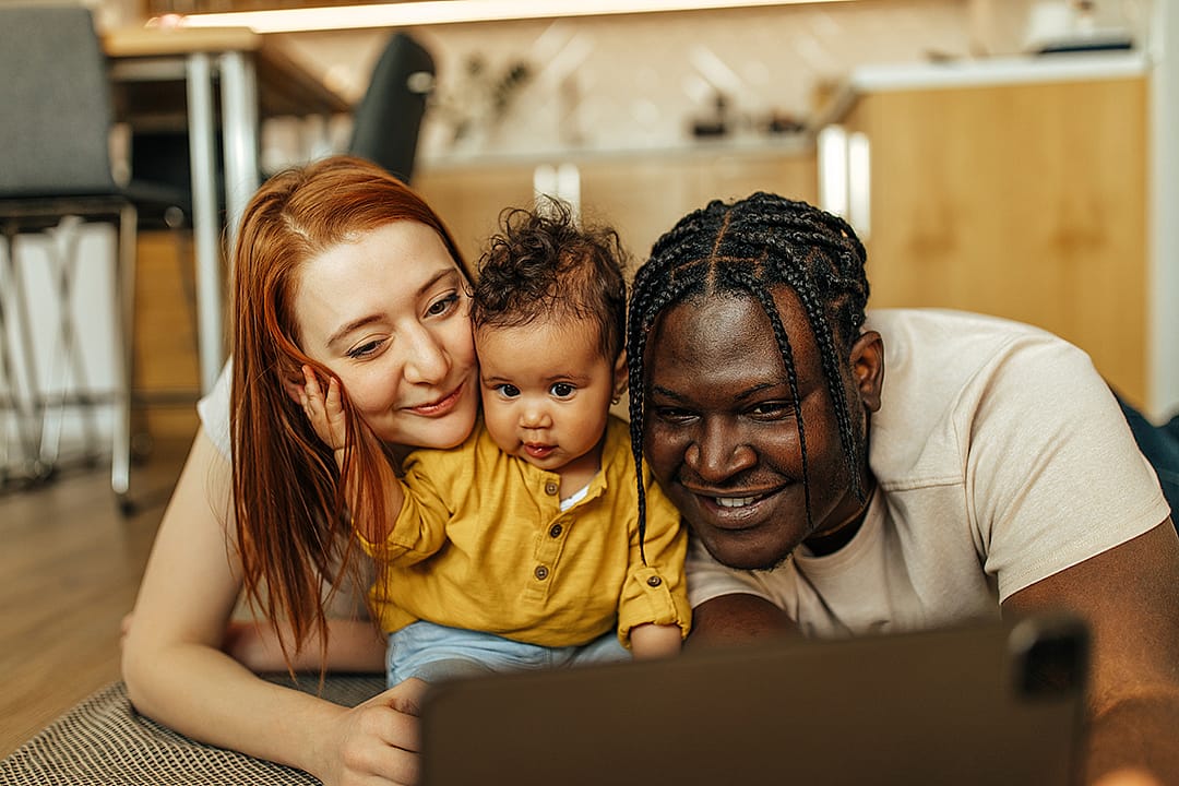 A happy couple with their young child watching something from a digital tablet.