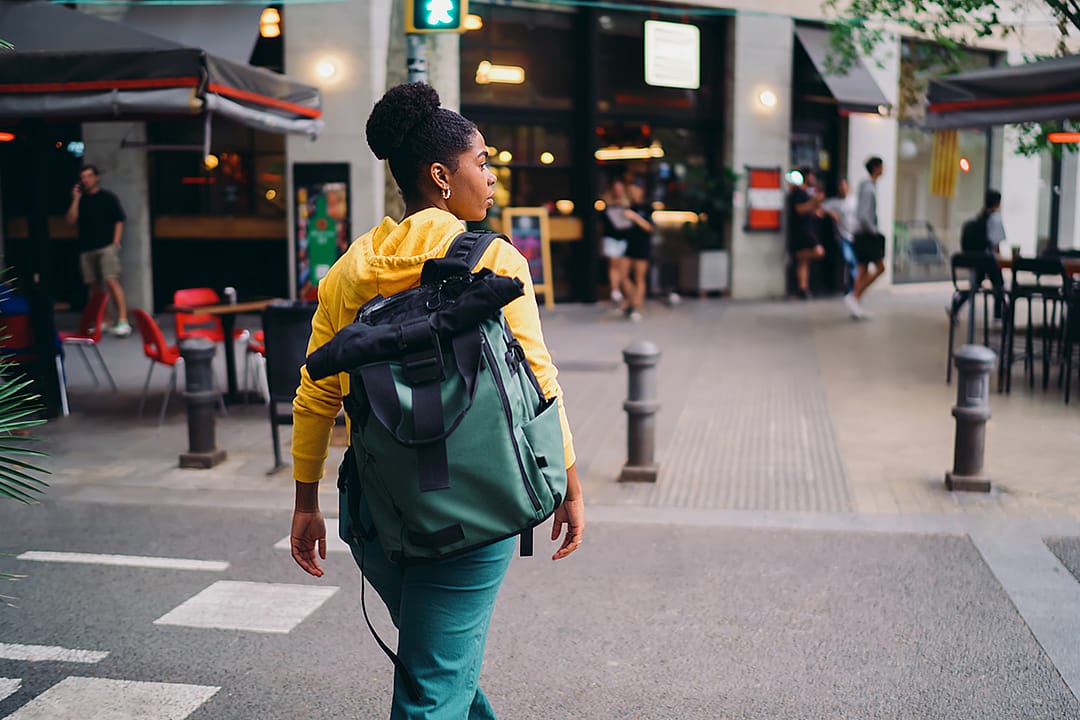 A woman with a backpack crossing a road.
