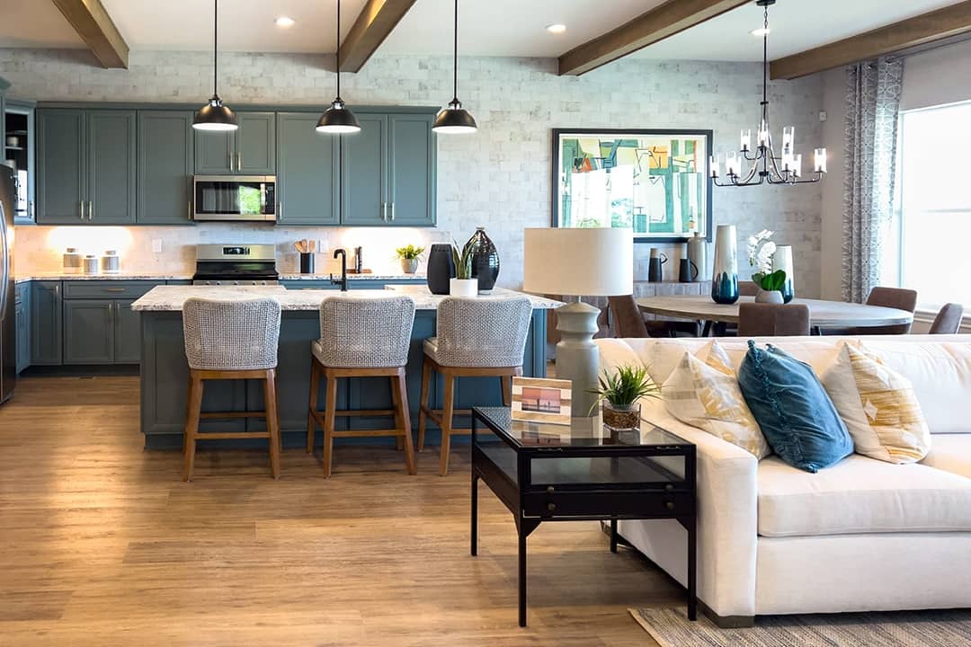 luxury open living space with cream-colored sectional, pillows, and kitchen in the background.