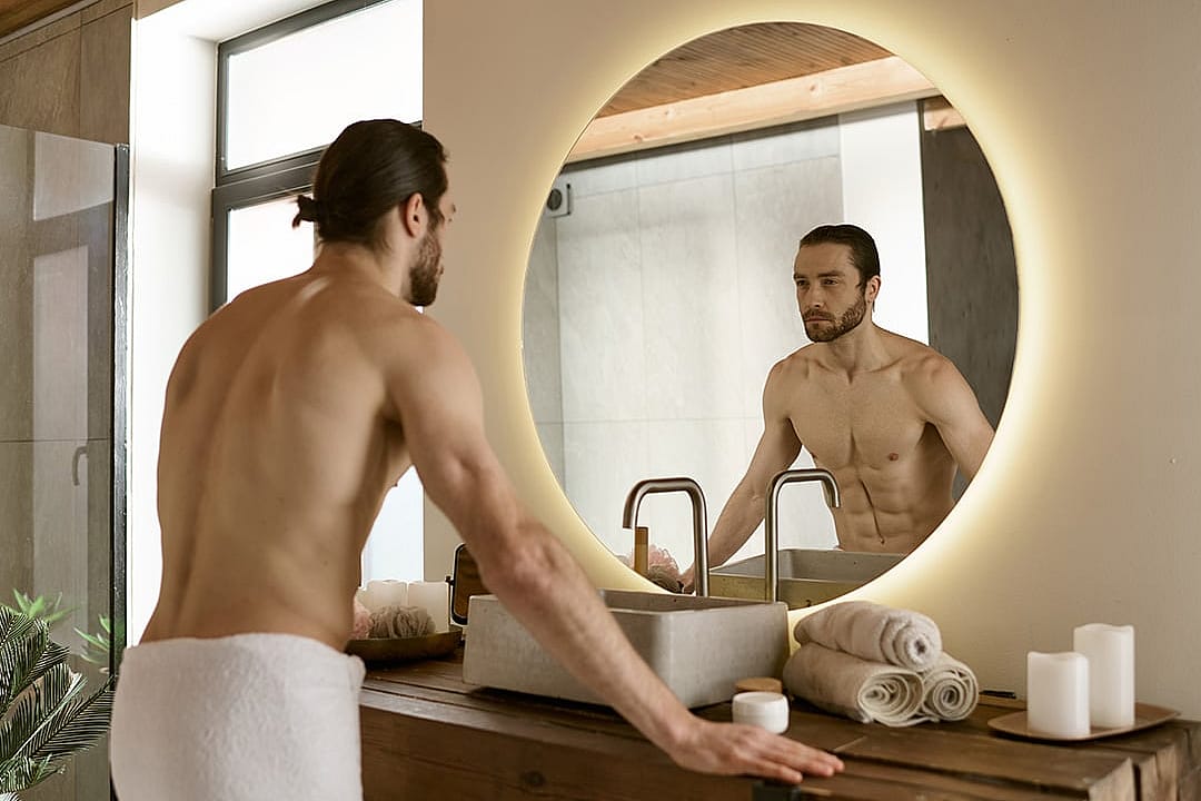 Man looking at himself in bathroom mirror while doing morning routine.