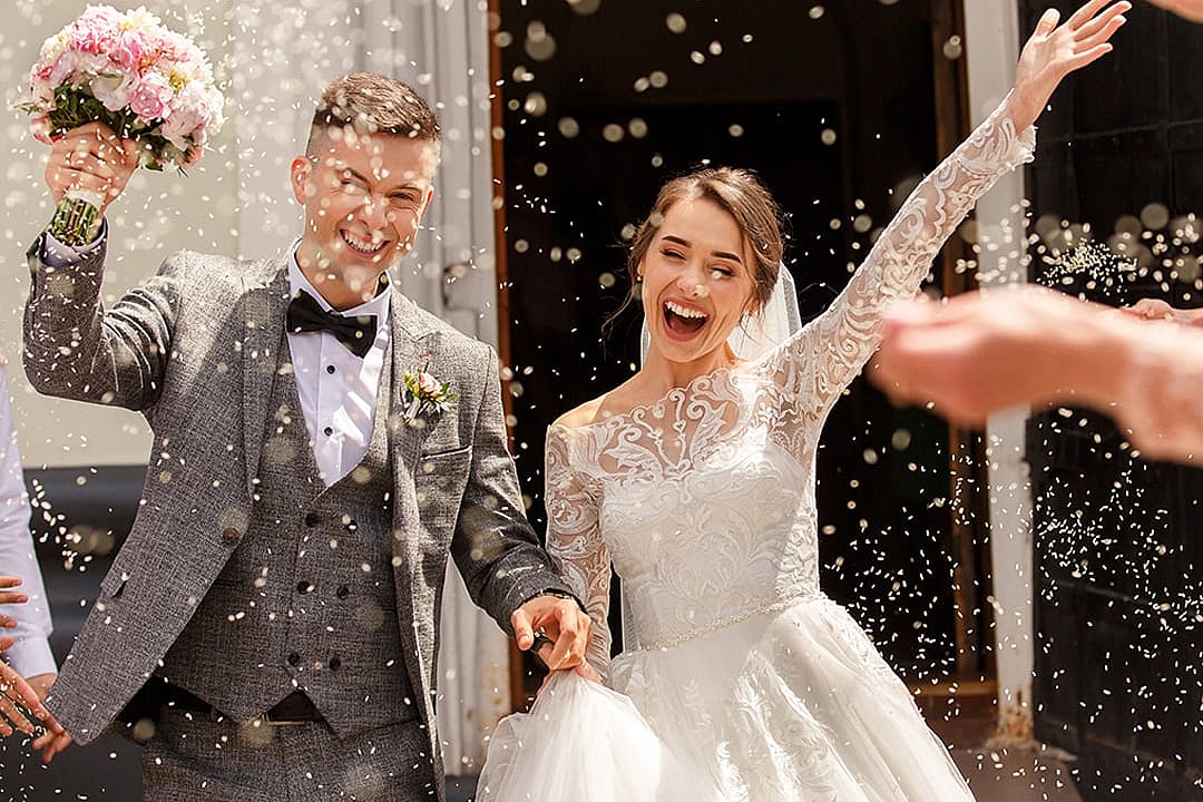 A newlywed couple celebrating after the ceremony while guests shower them with confetti.
