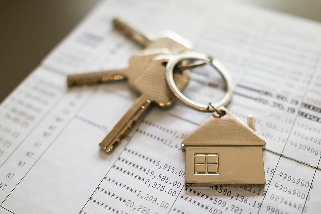 A keychain, house keys, and a bankbook in the background, representing a financial concept of cash flow for a home loan.