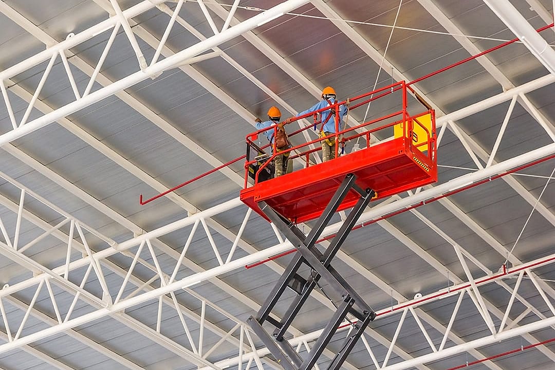 Construction workers doing a roof work in an elevated scissor lift platform with hydraulic system at a factory.