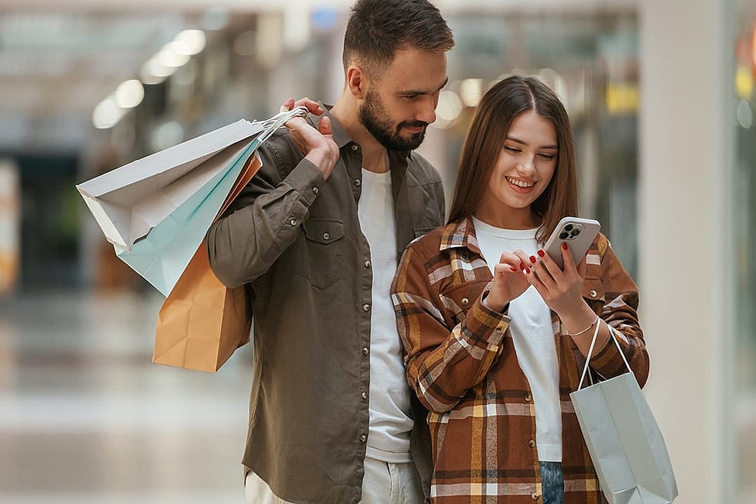 A young couple checking online special deals from a smartphone after shopping at the mall.