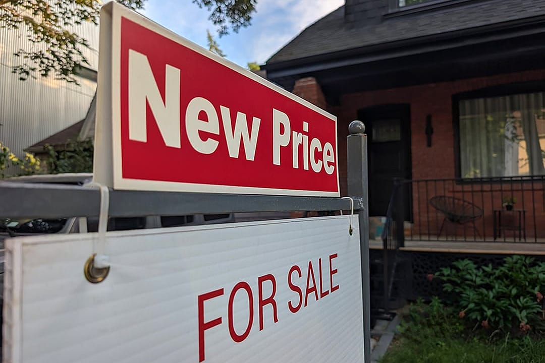 A sign for a new price sale displayed in a front yard of a single-detached residential house. 