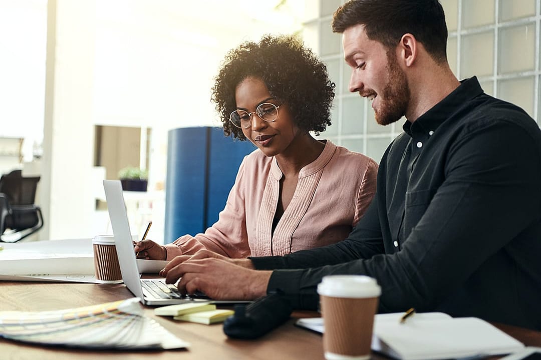 Two employees collaborating over financial data accounting and reviews from a laptop in an office.