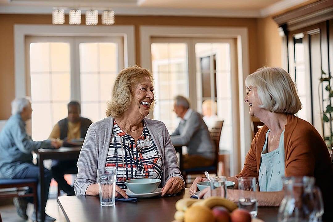 Elderly people enjoying a good conversation in the dining area of a nursing home.