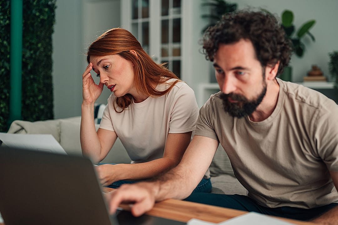 A couple at home feeling worried and stressed while calculating expenses.