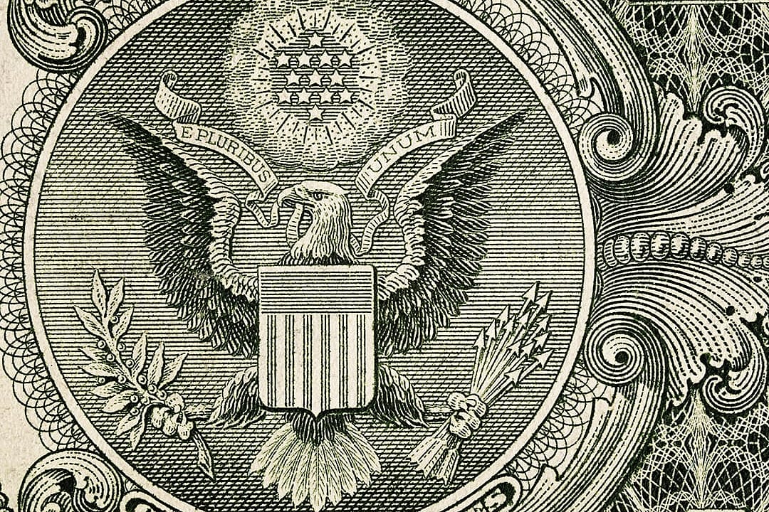 A close-up shot showing the macro details with the engraved eagle, shield, stars, and ornamental line work of the Great Seal of the United States on the one-dollar banknote.