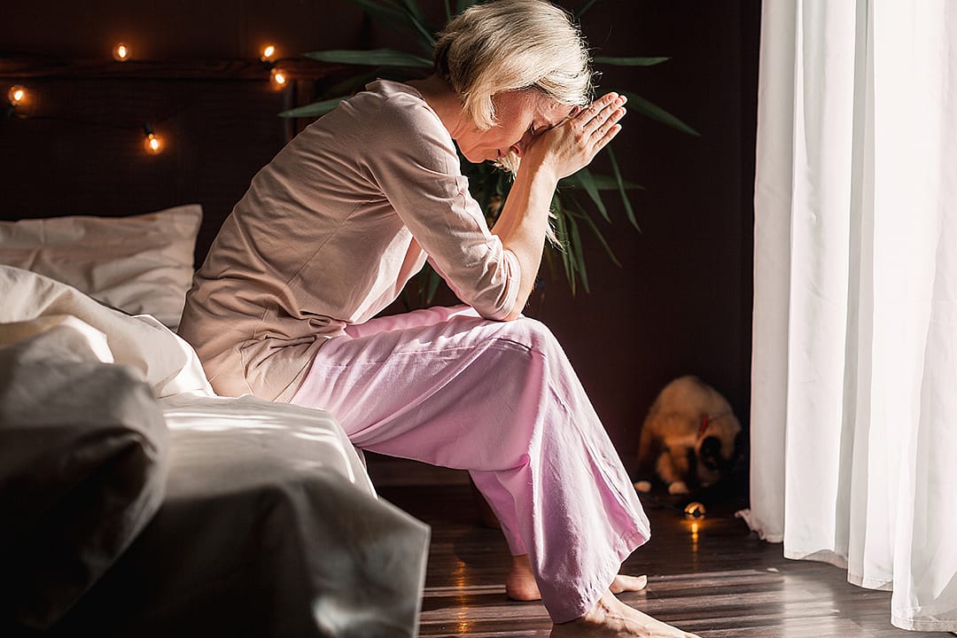 A stressed middle-aged woman sitting on her bed at home.