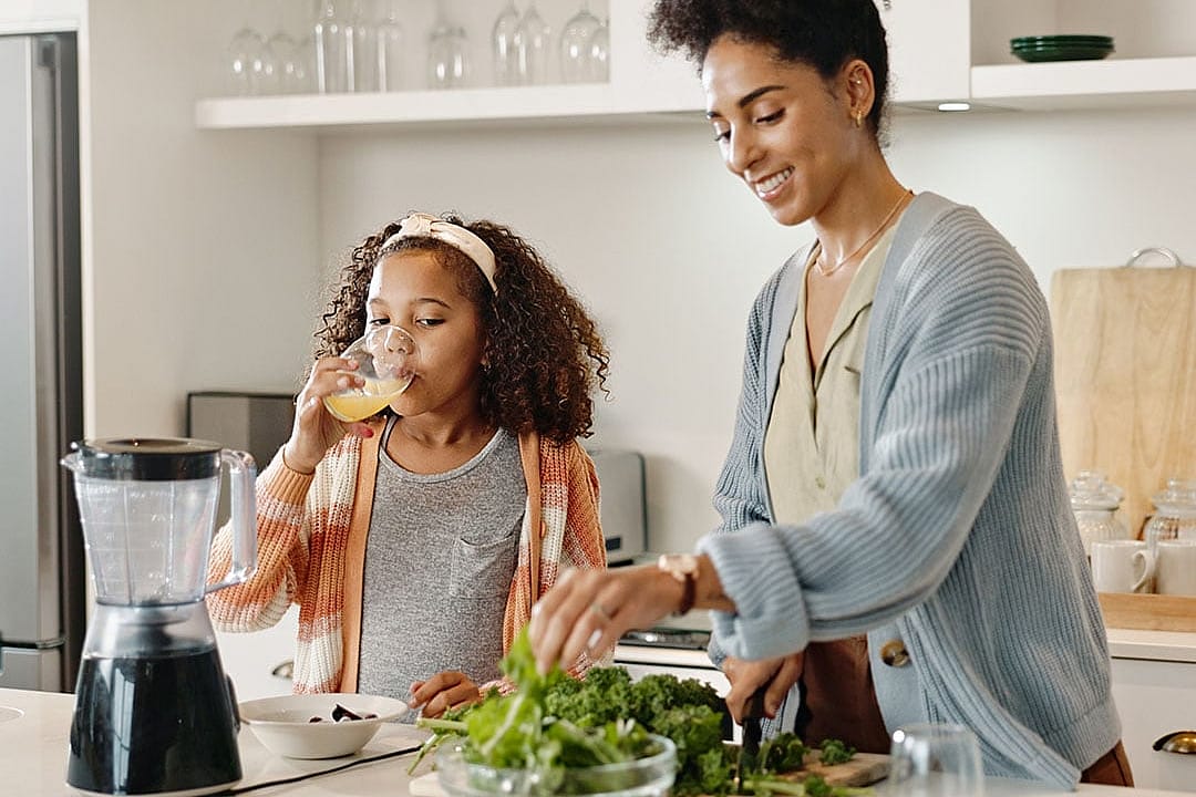 A mother prepares food with her young daughter in the kitchen.