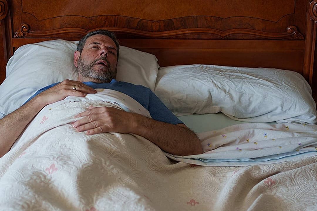 An elderly person sleeping on a bed and lying flat on their back.
