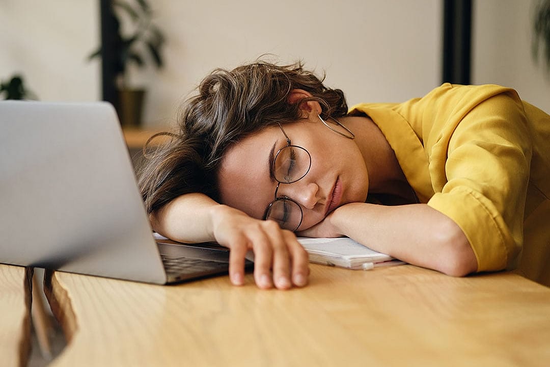 A tired young woman sleeping on a desk at work.