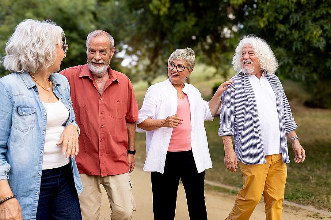 A group of elderly people enjoying a slow walk over happy conversations outdoors at the park.